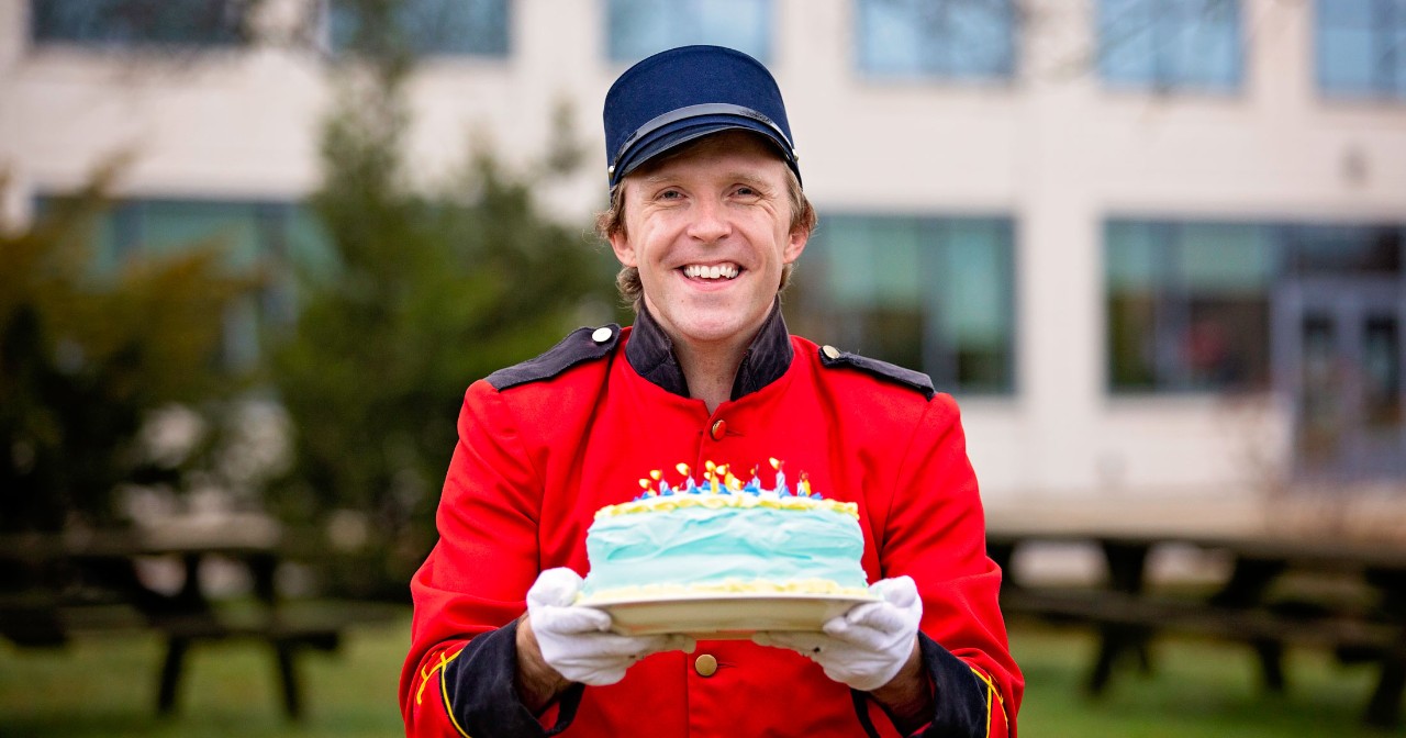 Taylor Darden wears a bellhop uniform and holds a birthday cake with flaming candles outside of STAR Campus