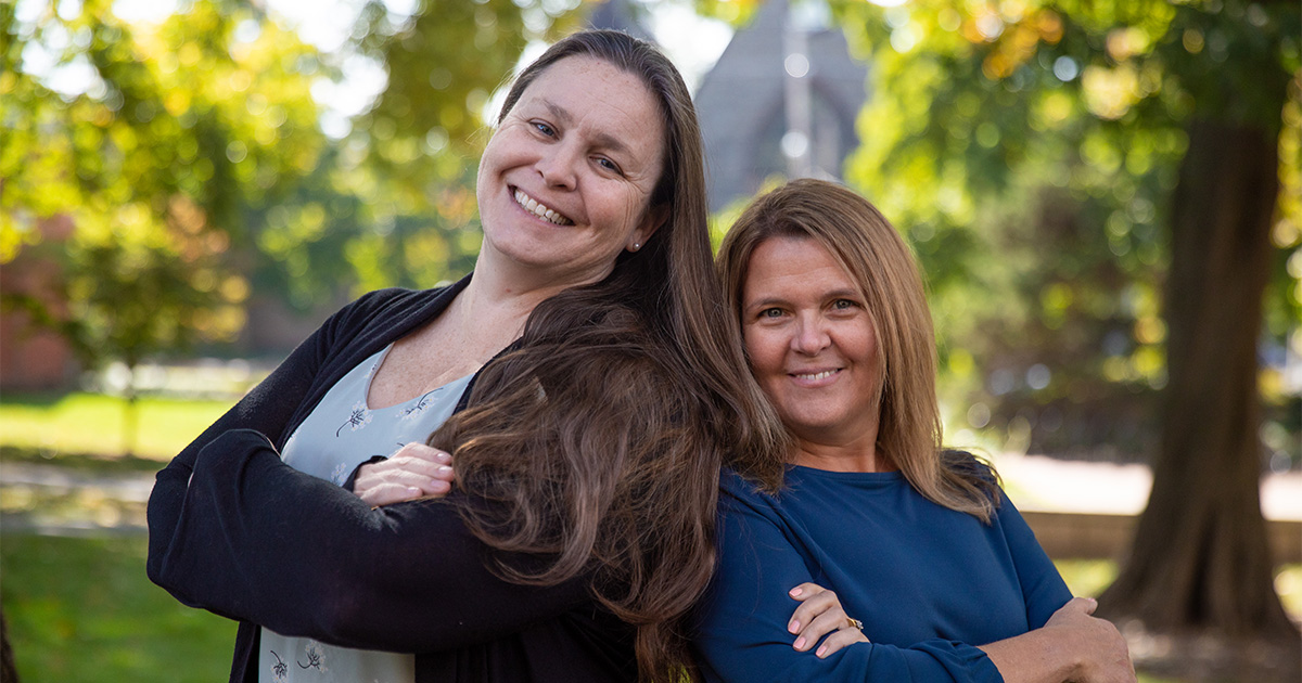 Two School of Nursing professors stand back to back with their arms crossed as they embark on a new educational partnership at Harvard.