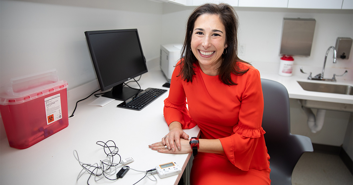 School of Nursing professor Lauren Covington poses in her lab with a sleep tracker worn on the wrist or ankle and a device that measures light for her research into sleep in socioeconomically disadvantaged families.