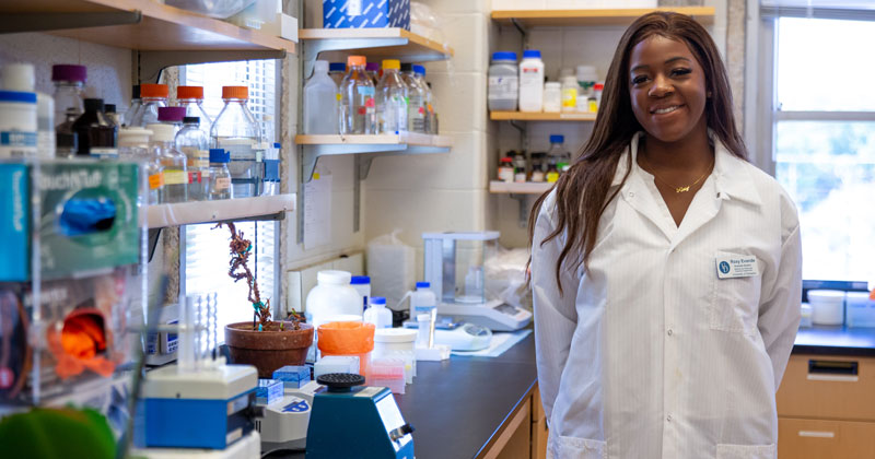 Woman stands next to counter with various science equipment