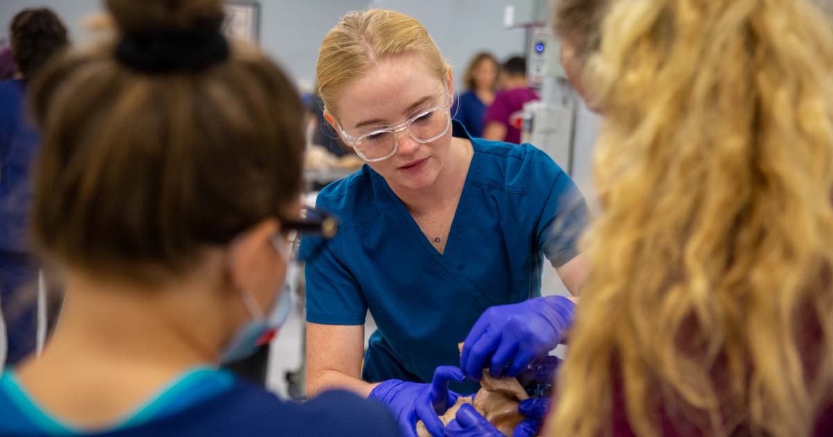 Three female students examine a donor body on a lab table