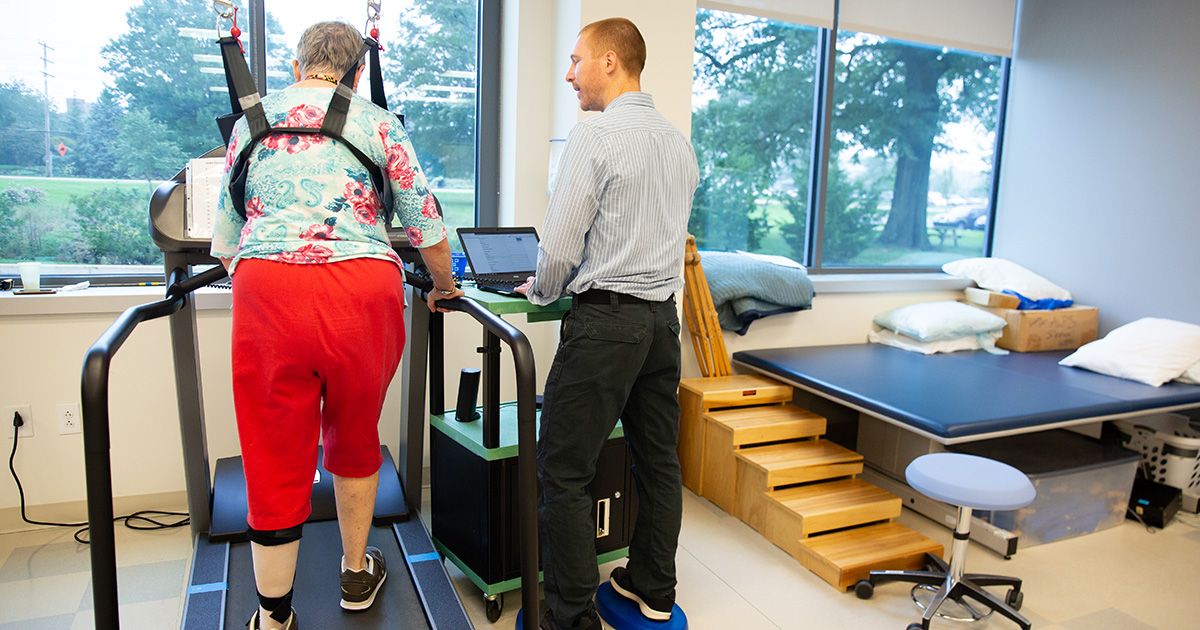 A woman who survived a stroke walks on a treadmill as part of her physical therapy.