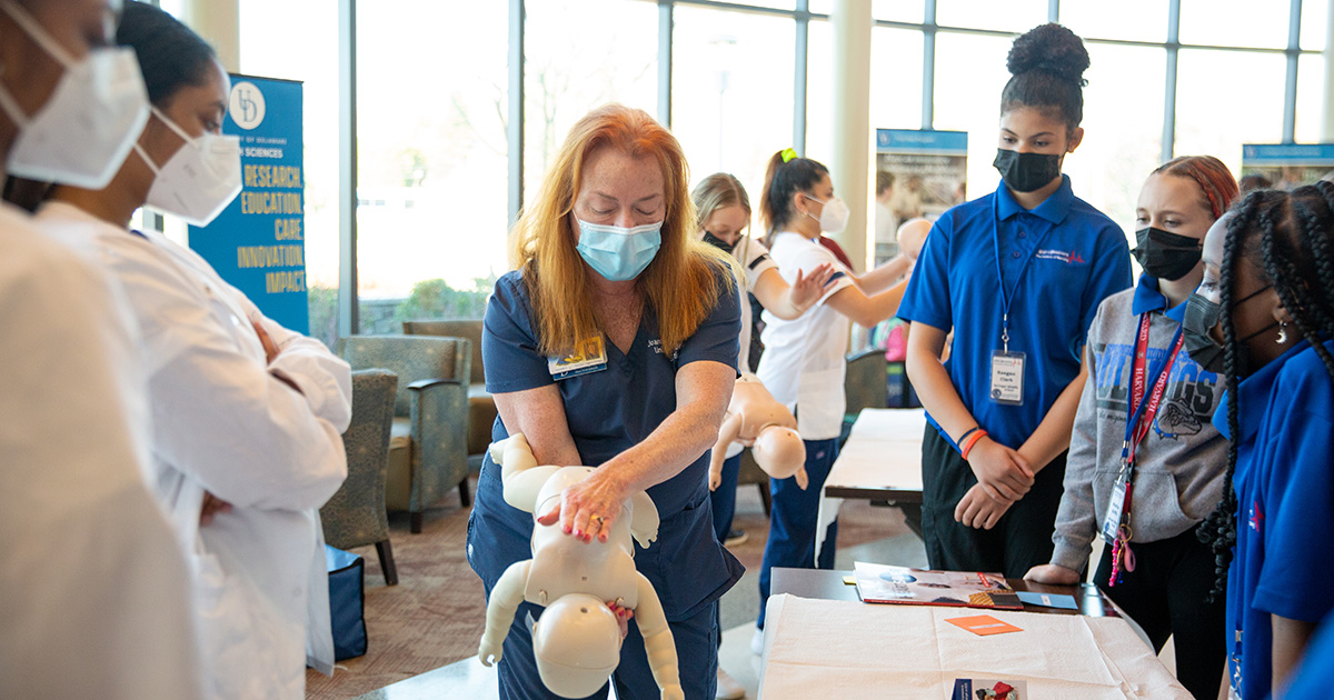 A School of Nursing instructor shows middle school students how to perform CPR on a baby using a mannequin. 