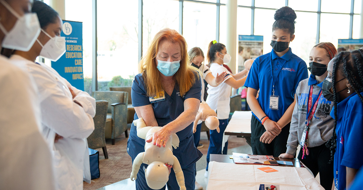 A School of Nursing instructor shows middle school students how to perform CPR on a baby using a mannequin.