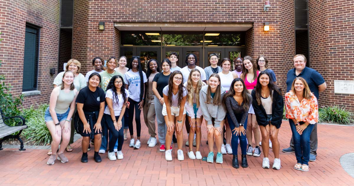23 students, faculty, and staff gathered for a group photo outside of the nursing building