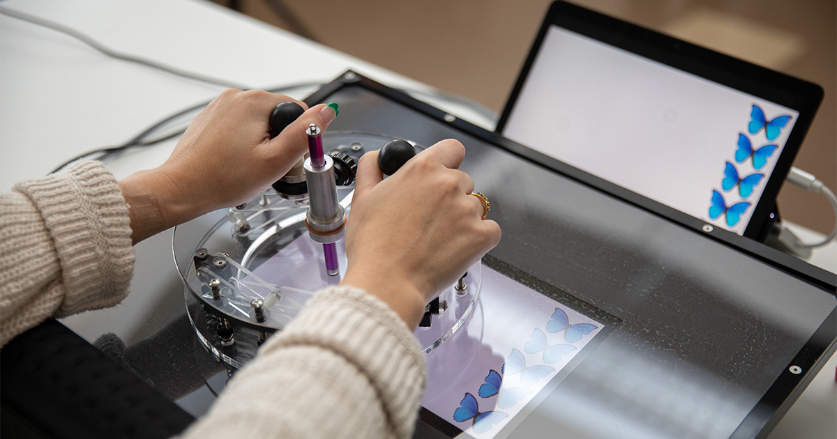 A student pilots an assistive drawing device for people with upper limb disabilities who lack fine motor skills, giving them the ability to draw. Here, she's playing a game with blue butterflies on the screen.