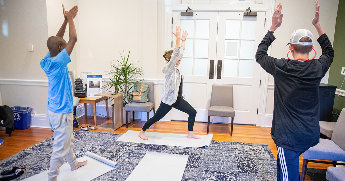 Two students participate in yoga with an instructor as a way to provide stress relief and improve mental health.