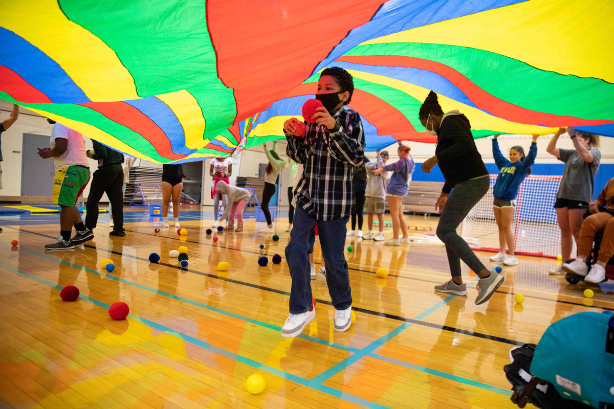 Young children under a colorful parachute in a gym class