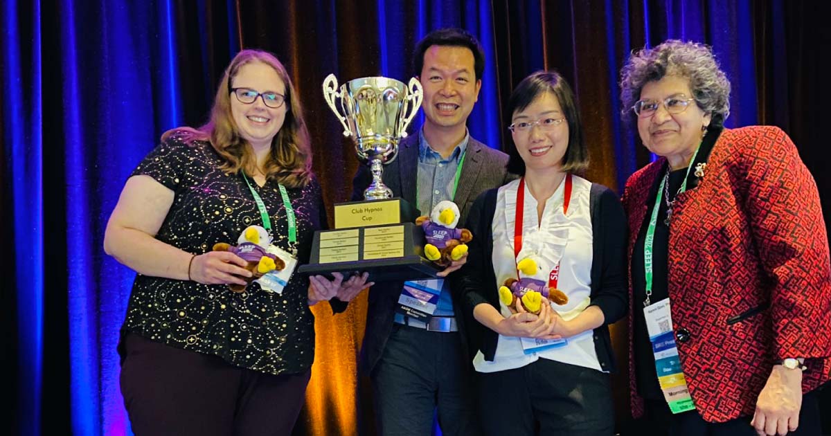 Four professionals gather for photo holding a large cup award on stage 