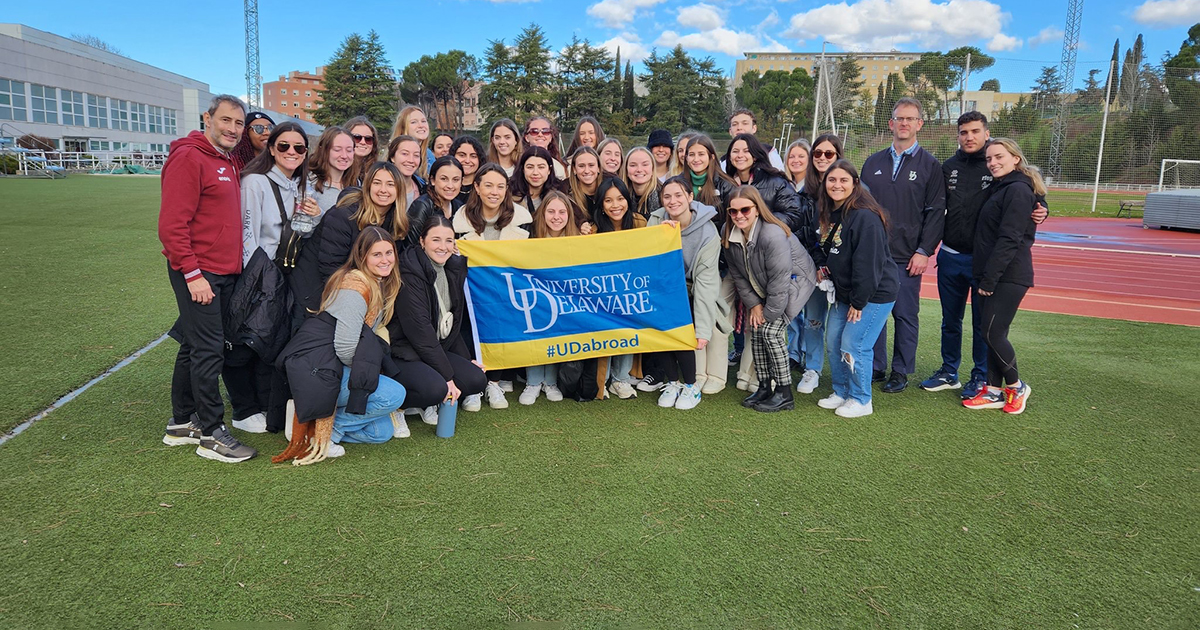 Students from the University of Delaware’s College of Health Sciences and the College of Arts and Sciences hold a UD banner outside an Olympic Training Center in Madrid during a Winter Session study abroad. 