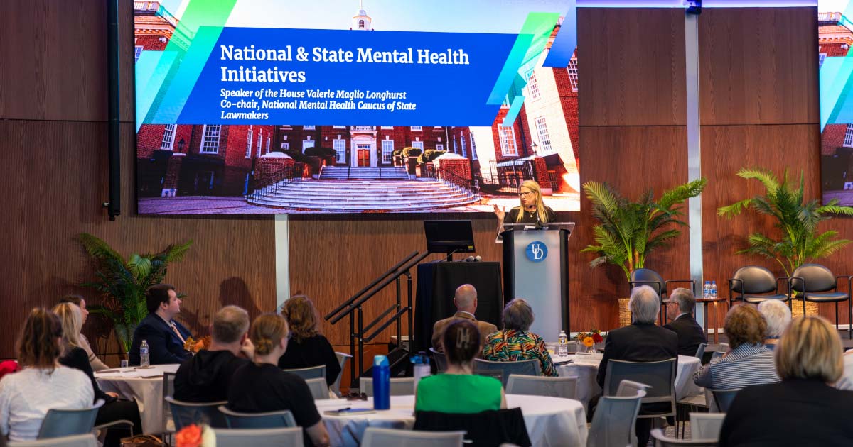 Woman standing at a podium giving a presentation as part of a huge symposium event 