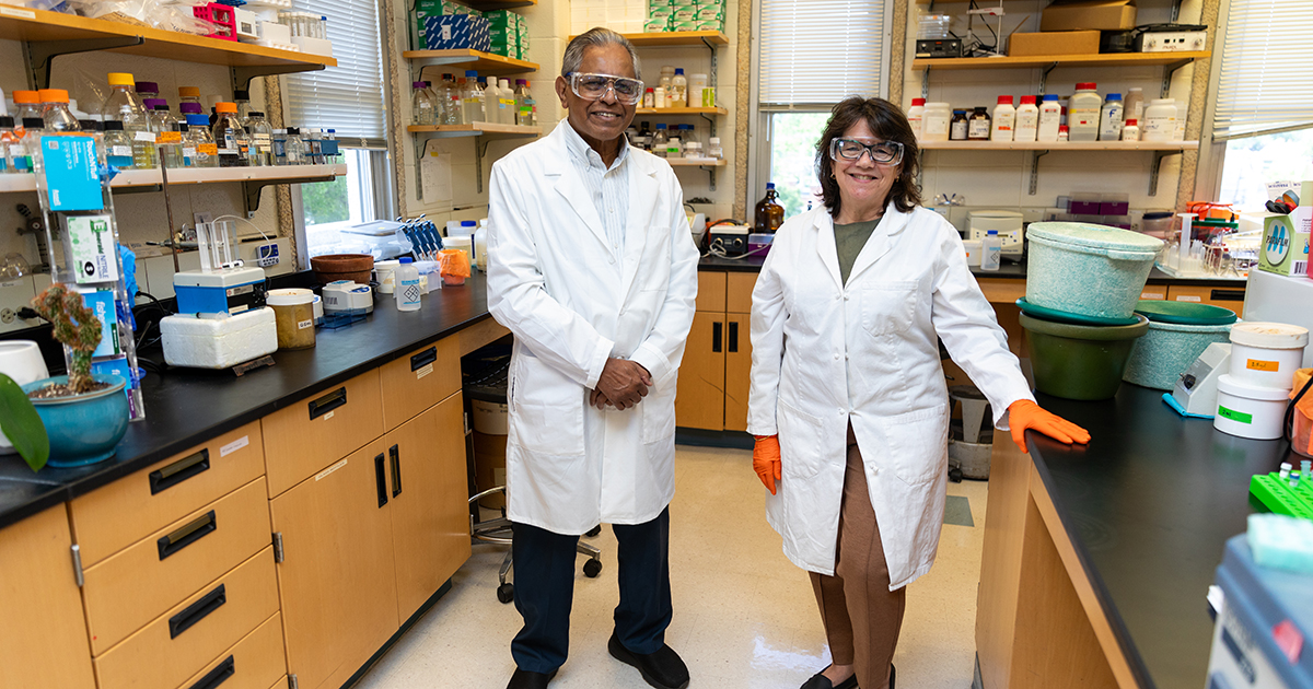 University of Delaware medical and molecular sciences professors Sam Biswas and Esther Biswas-Fiss pose in white lab coats and goggles in their lab where they conduct HPV research.