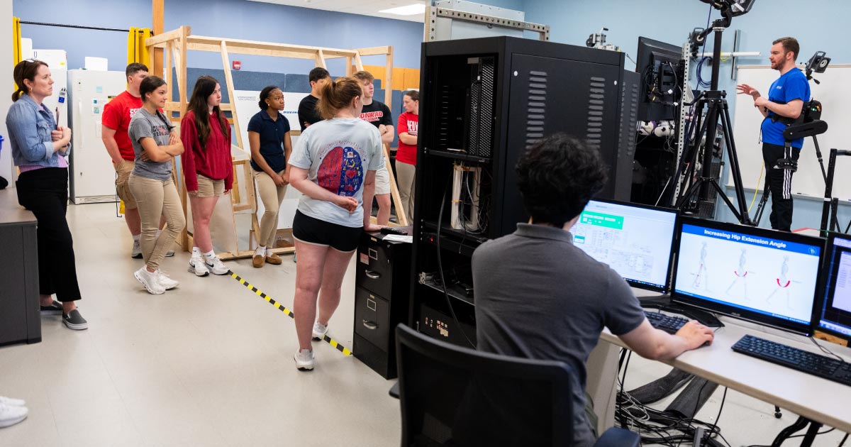 A group of high school students observe a college graduate student showcasing how human robotics work