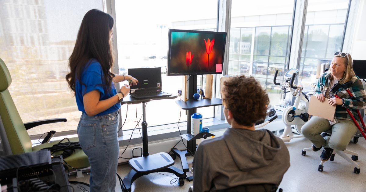 A female college graduate student shows a high school student in a wheel chair how motor neuroscience works