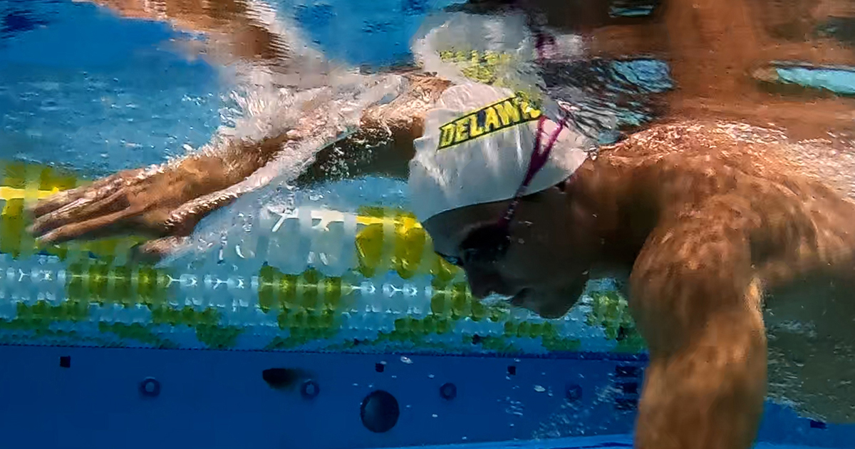 An underwater shot of men swimming underwater wearing UD swim caps in UD's Lil Bob pool. 