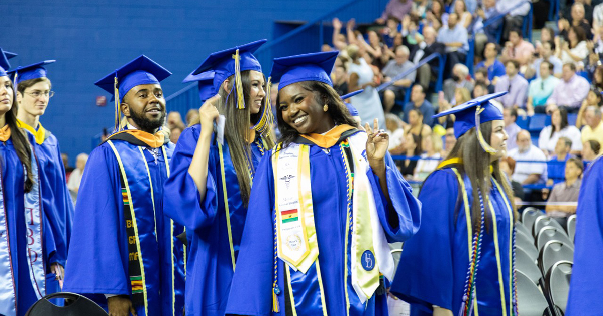 Seniors smile, wearing their blue cap and gowns at the 2024 UD CHS Convocation. 