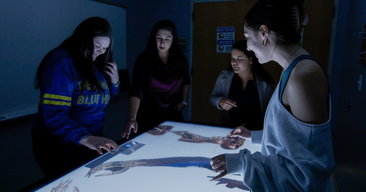 Students in a dark room use Toltech virtual anatomy tables (basically giant iPads) to explore anatomy in 3D