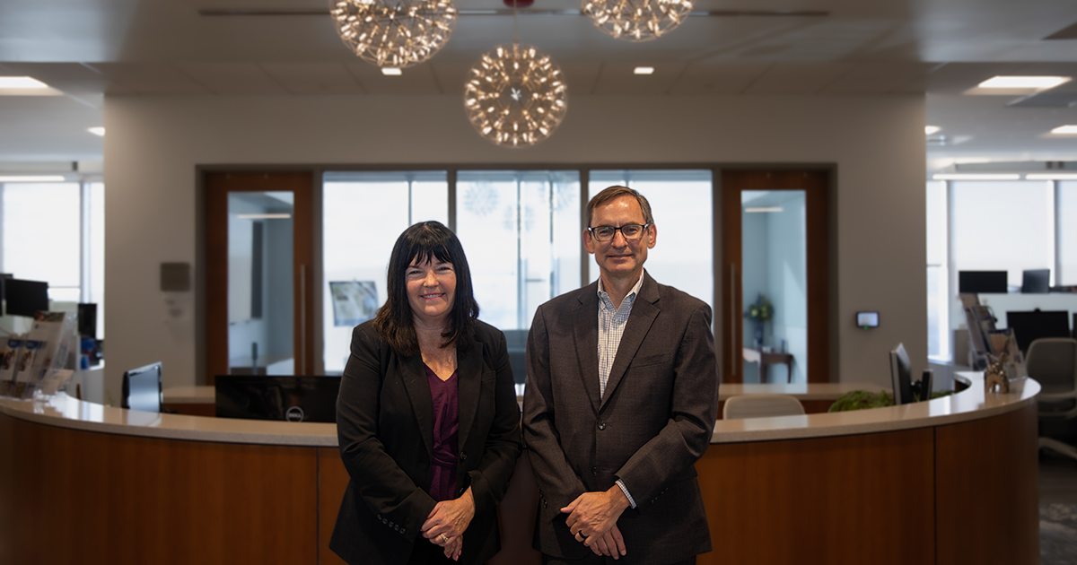 State Rep. Kim Williams (L) poses with College of Health Sciences Dean Bill Farquhar (R) in the lobby of the Dean's Office with a circular receptionist desk behind them. 