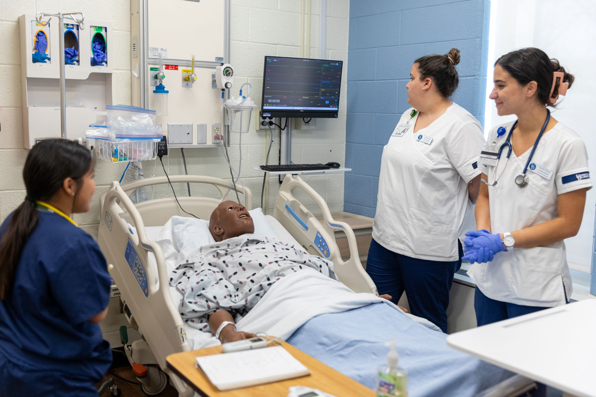 Nursing students and faculty gathered around a test patient in a hospital bed