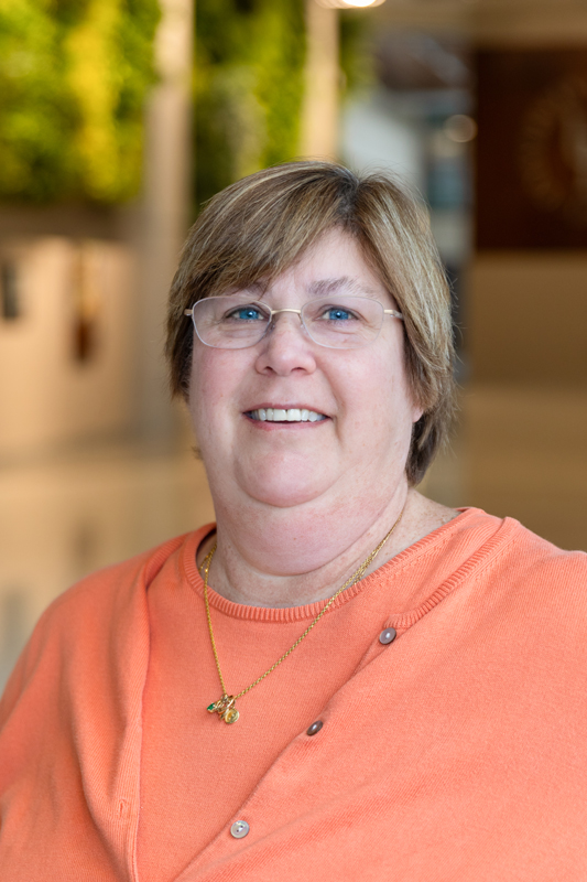 A headshot of new Physical Therapy Associate Professor Sheri Silfies wearing glasses and an orange shirt taken in the STAR Tower lobby.