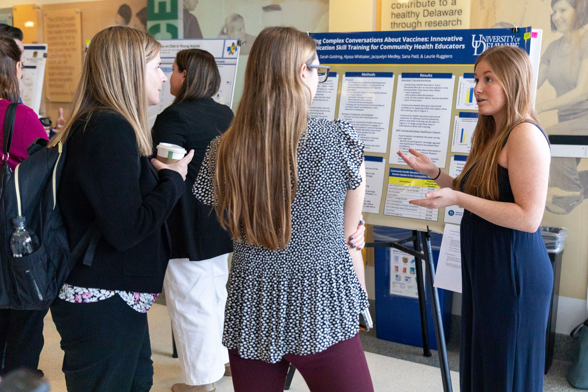 Sydney Bouder, a second-year student in the master of health promotion and health coaching program, stands in front of her research poster while talking to Research Day attendees.