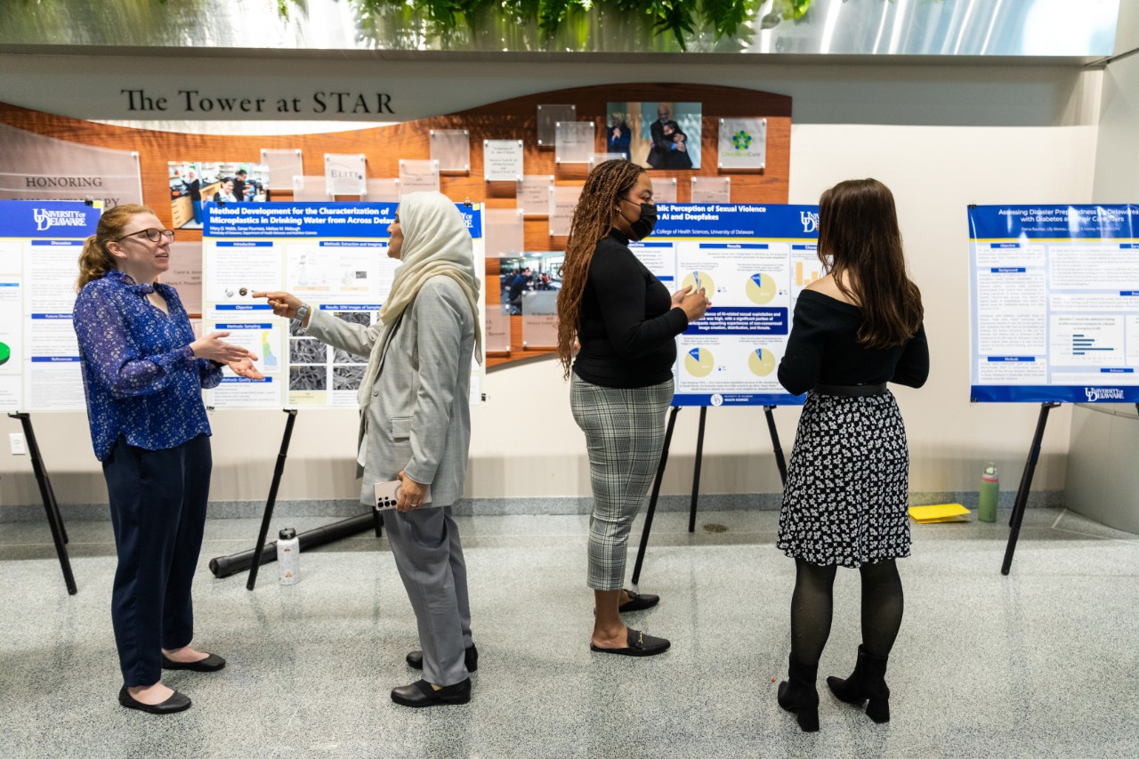 Taylor Burton (center), a second-year student in the master of public health in epidemiology program, presented research on public perceptions of AI-facilitated sexual violence using deep-fake technology.  Here, she's in the center talking to a Research Day attendee. To her, left is another poster with a student talking to an attendee about her research.