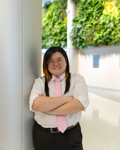 Percival Tran stands with arms crossed leaning against a pole with the Living Wall in the STAR Atrium in the background.