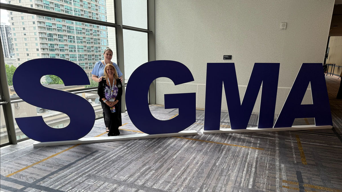 An image of two women posing as the letter "i" in giant letters that spell out Sigma