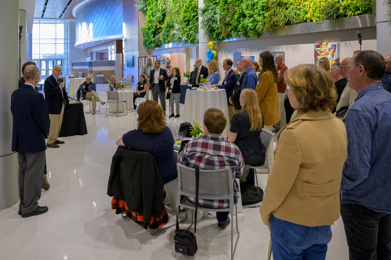 People crowd around speakers in the STAR Atrium Lobby with the Living Wall of greenery above them. for the naming of the arlow-Rose Center for Anatomy and Physiology Education.