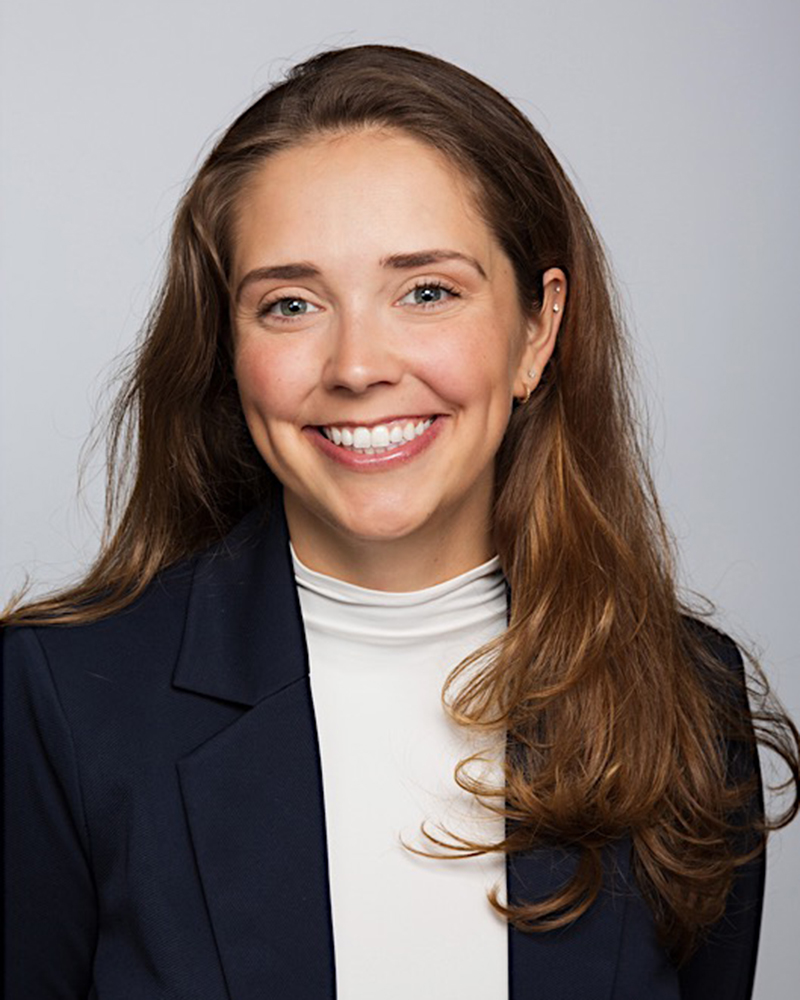 A headshot of Devon Tapp wearing a black blazer and white mock turtleneck. 