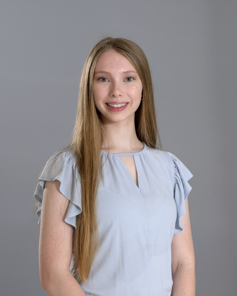 A headshot of Abigail McLaughlin, a senior medical diagnostis major, wearing a short sleeve ruffled light blue shirt with her hands clasped.