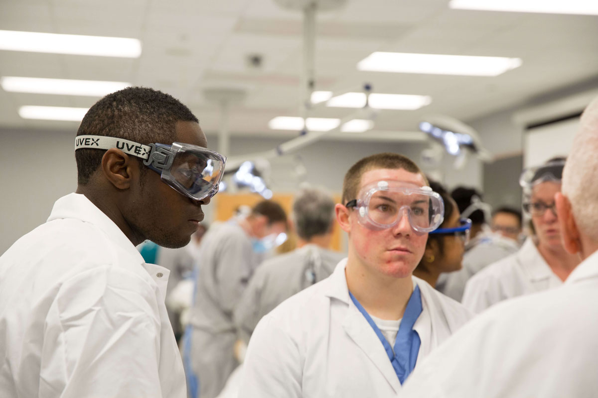 Multiple students in lab glasses and lab coats in the human anatomy lab