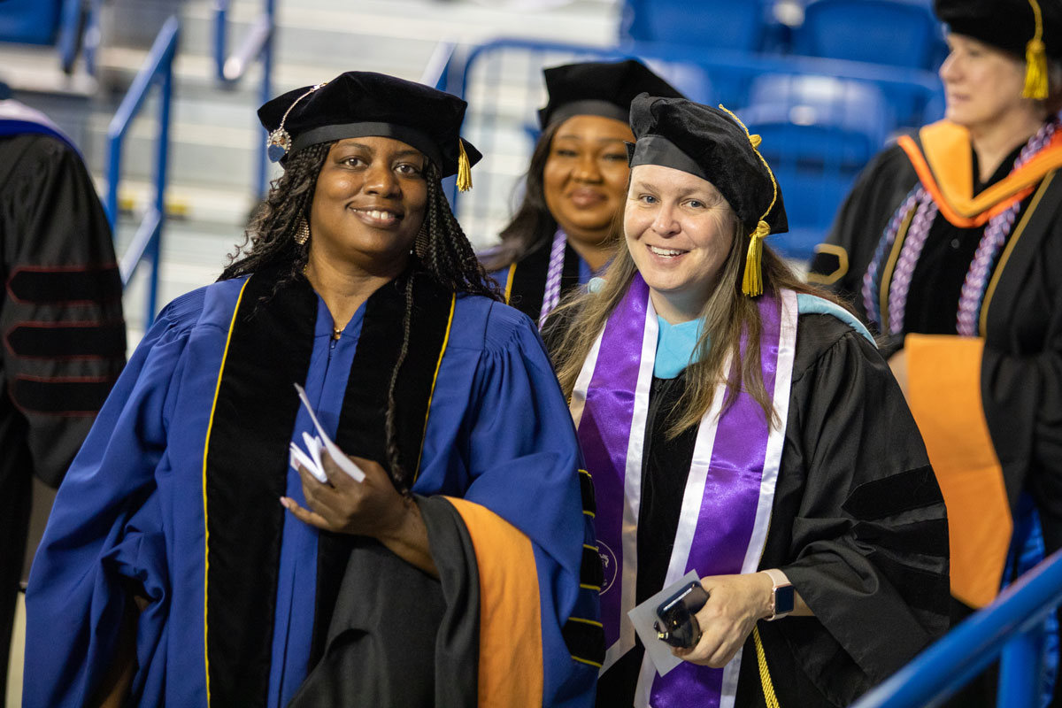 Graduate Hooding Ceremony with two individuals in docorate robes smiling at the camera.