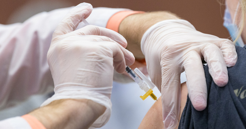 Gloved hands holding a vaccine needle and pinching skin on the upper arm of a patient