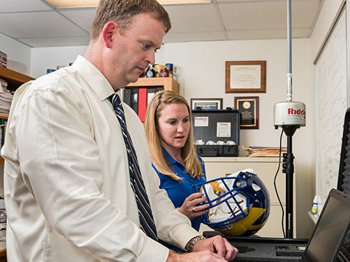 Tom Buckley, assistant professor of Kinesiology and Applied Physiology, and PhD student Jessie Oldham working with a football helmet containing sensors designed to measure and track impacts players' heads during practices and games.