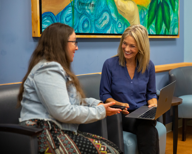 Two women sitting, talking while looking at a laptop