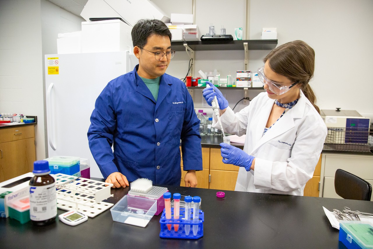 Two individuals pipetting samples into test tubes in a lab