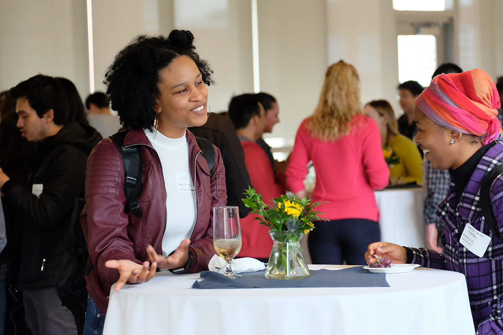 2 Graduate students smiling and having a conversation at a networking event.