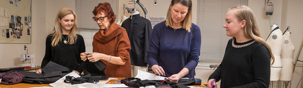 Fashion and apparel students and instructors stand around a table as they work on projects.