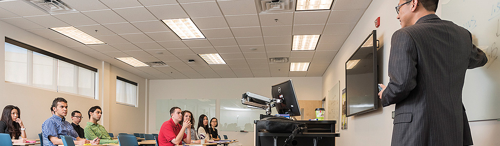 Financial Services Analytics Students in class while an instructor is teaching the at front of the classroom.