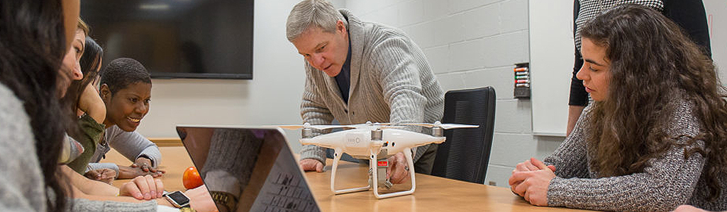 A professor and students in a classroom discussing a drone being used for research.