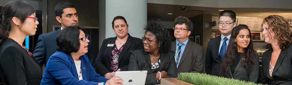 Hospitality business management students dressed professionally as they listen to an instructor in a hotel lobby.