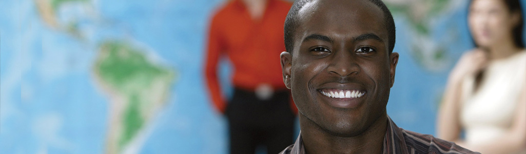 International business student smiling in foreground with a map of the world behind him.