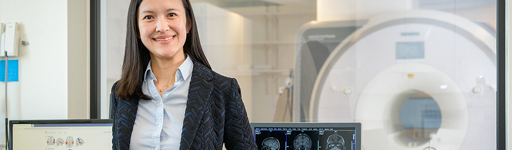 Linguistics & Cognitive Science A researchers smiles in front of an MRI with brain scans on the computer behind her.