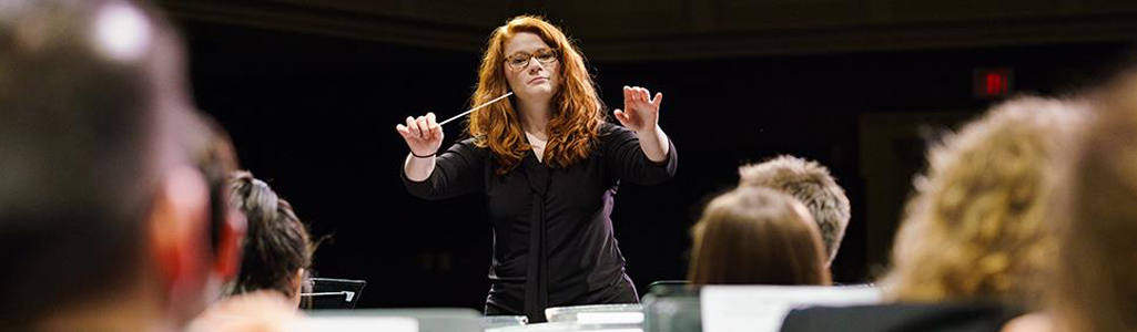 A student with arms raised as she conducts musicians.