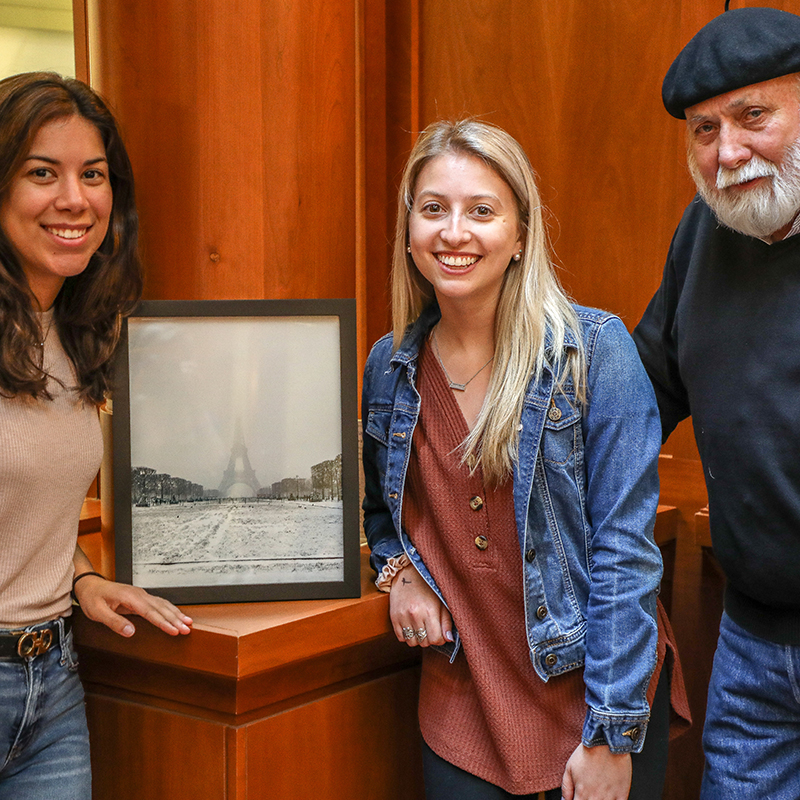 Two students and a faculty member stand next to a winning entry in the 2019 photo contest