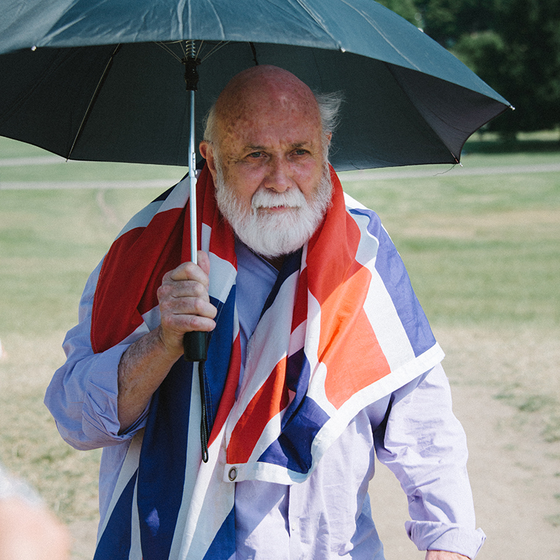 Faculty Director Bill Deering holds an umbrella and wears a British Flag across his shoulders.
