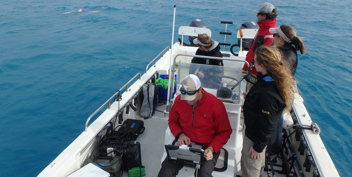 Students and a professor sit on a boat and do research.