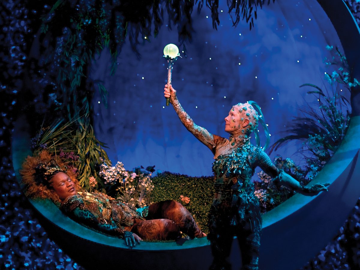 Two performers in elaborate floral costumes perform during a play. Two performers in elaborate floral costumes perform during a play.