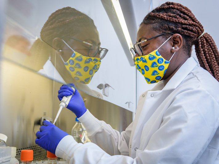 A young woman in a mask performs a laboratory experiment with a pipette.